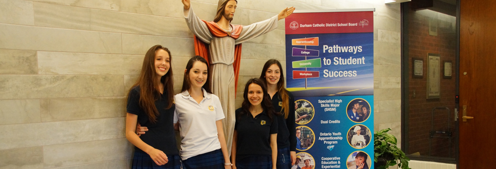 Female students standing by Pathways banner and statue of Jesus