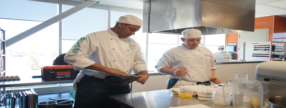 Two male students in chef outfits in a kitchen